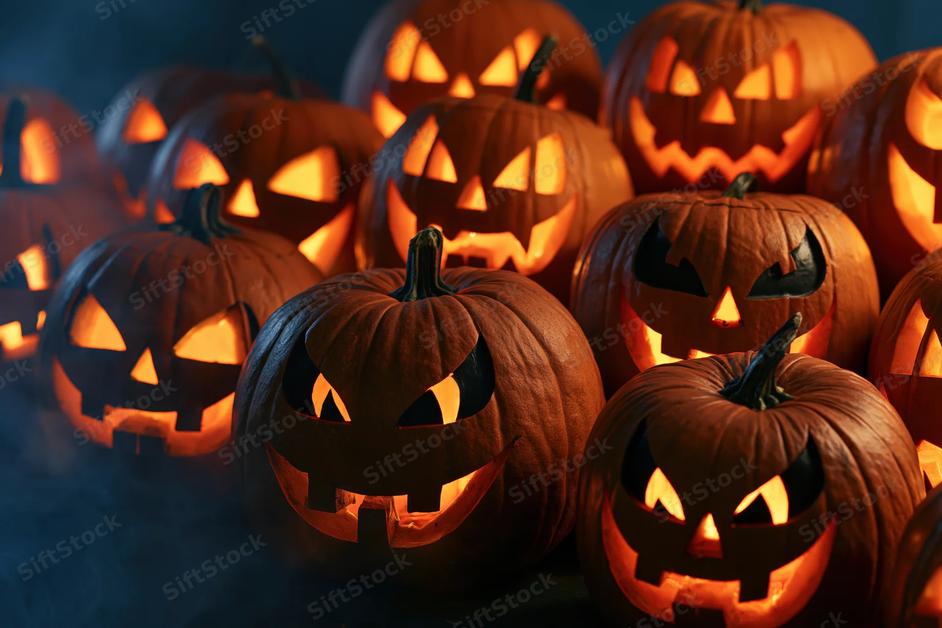 Cluster of carved jack-o-lanterns glowing in the dark with smoke swirling around