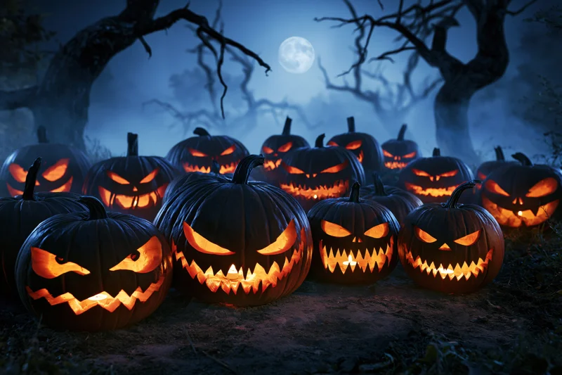 Carved jack-o-lanterns glowing in a dark forest at night under a full moon