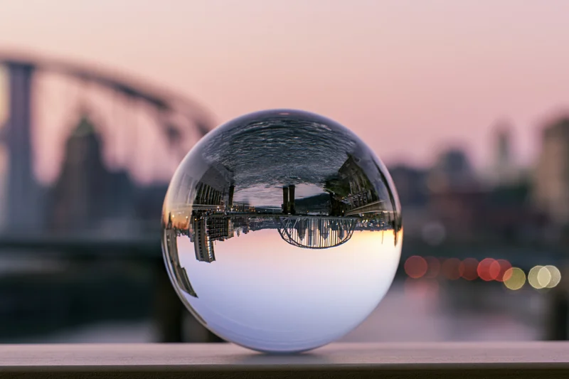 Crystal lensball reflecting inverted cityscape and bridge at dusk on a railing
