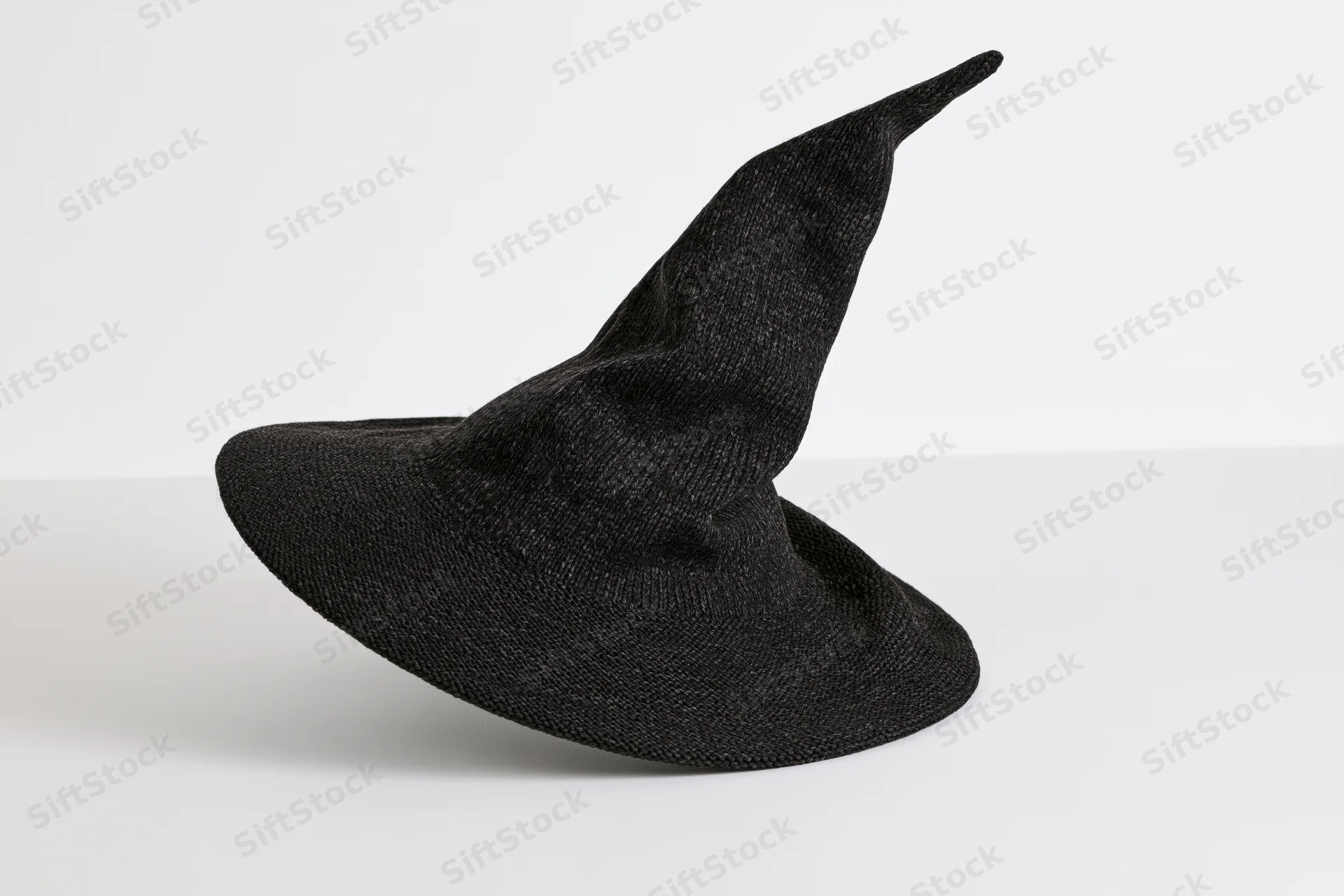Dark charcoal knitted witch hat with asymmetric point resting on white surface
