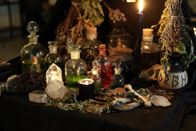 Dark ritual altar with candles, glass bottles, herbs, bones, crystals and a skull on black cloth