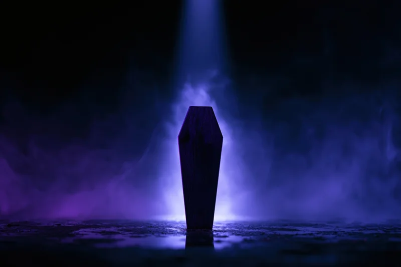 Dark wooden miniature coffin standing upright on wet reflective surface in foggy blue-lit scene