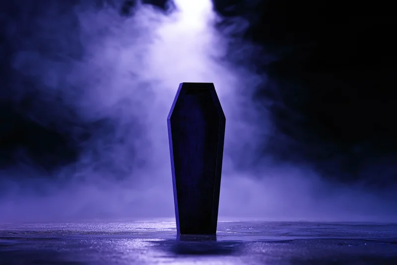 Dark wooden miniature coffin standing upright on wet reflective surface in purple smoke