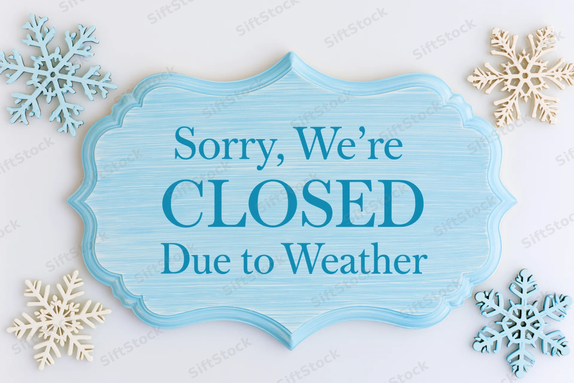 Blue wooden sign reading sorry were closed due to weather surrounded by snowflakes on white background