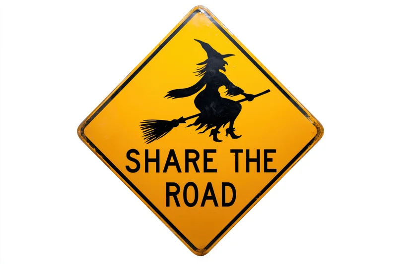 Diamond-shaped yellow road sign with black witch silhouette on broom and text share the road isolated on white