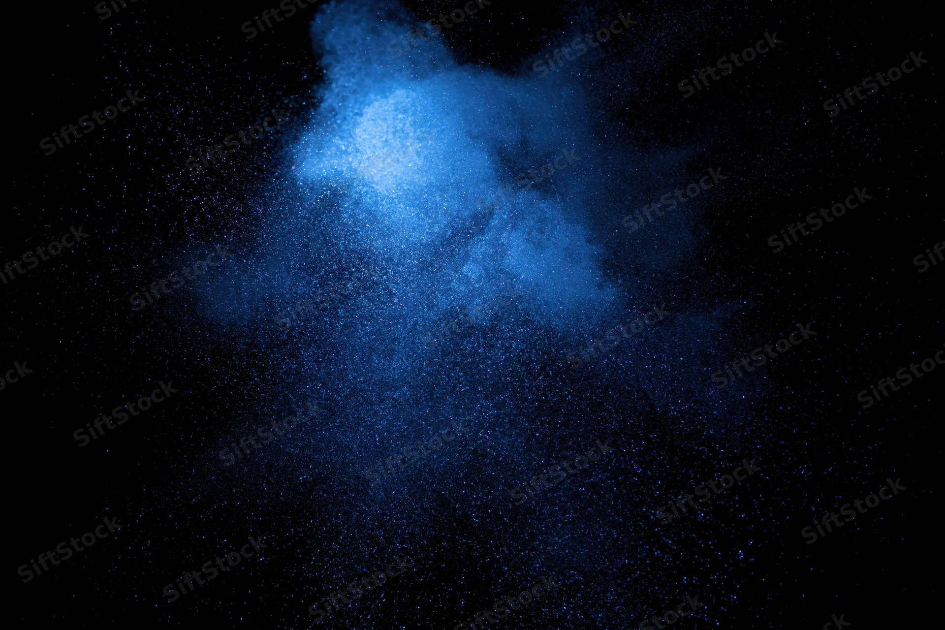 Blue powder cloud suspended in dark space with glowing particles dispersing mid-air