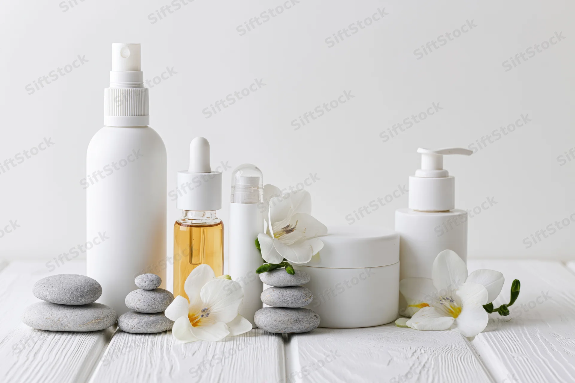 White minimalist skincare products arranged with lilies and stones on a wooden table