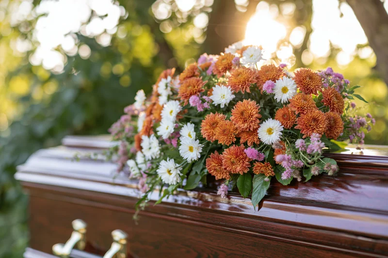 Floral arrangement of orange chrysanthemums and white daisies on a polished wooden coffin outdoors in a cemetery