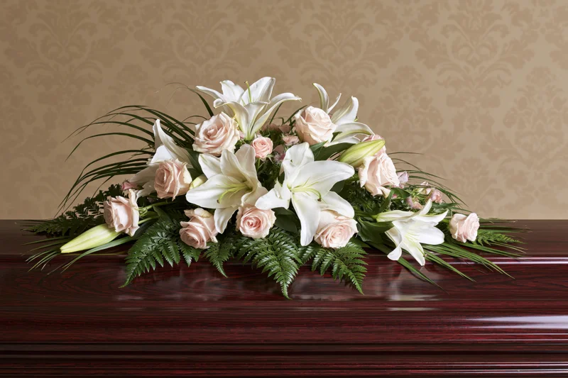 Floral arrangement of white lilies and pink roses on a dark wooden coffin