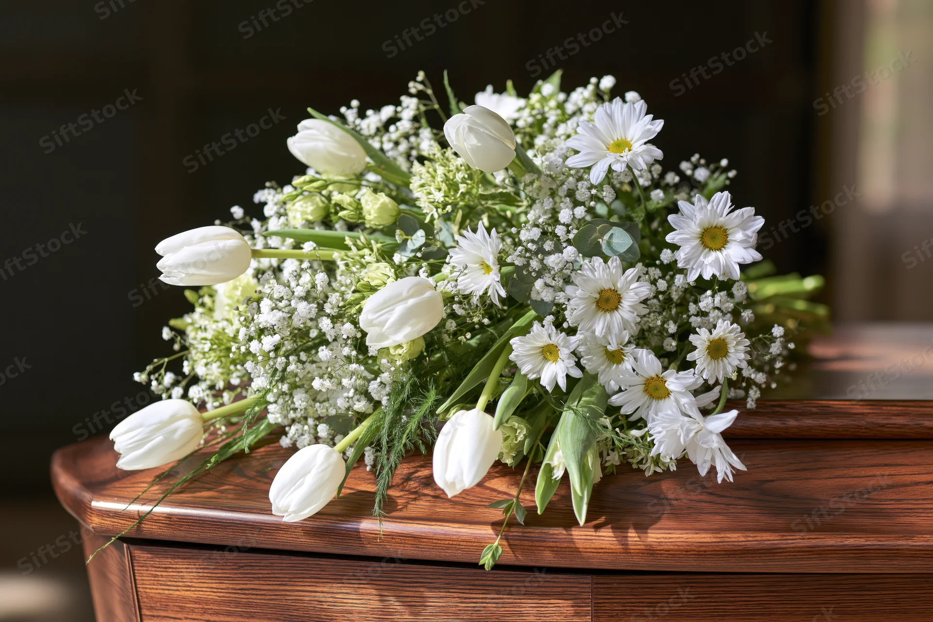 White tulips and daisies arranged with gypsophila on a wooden coffin