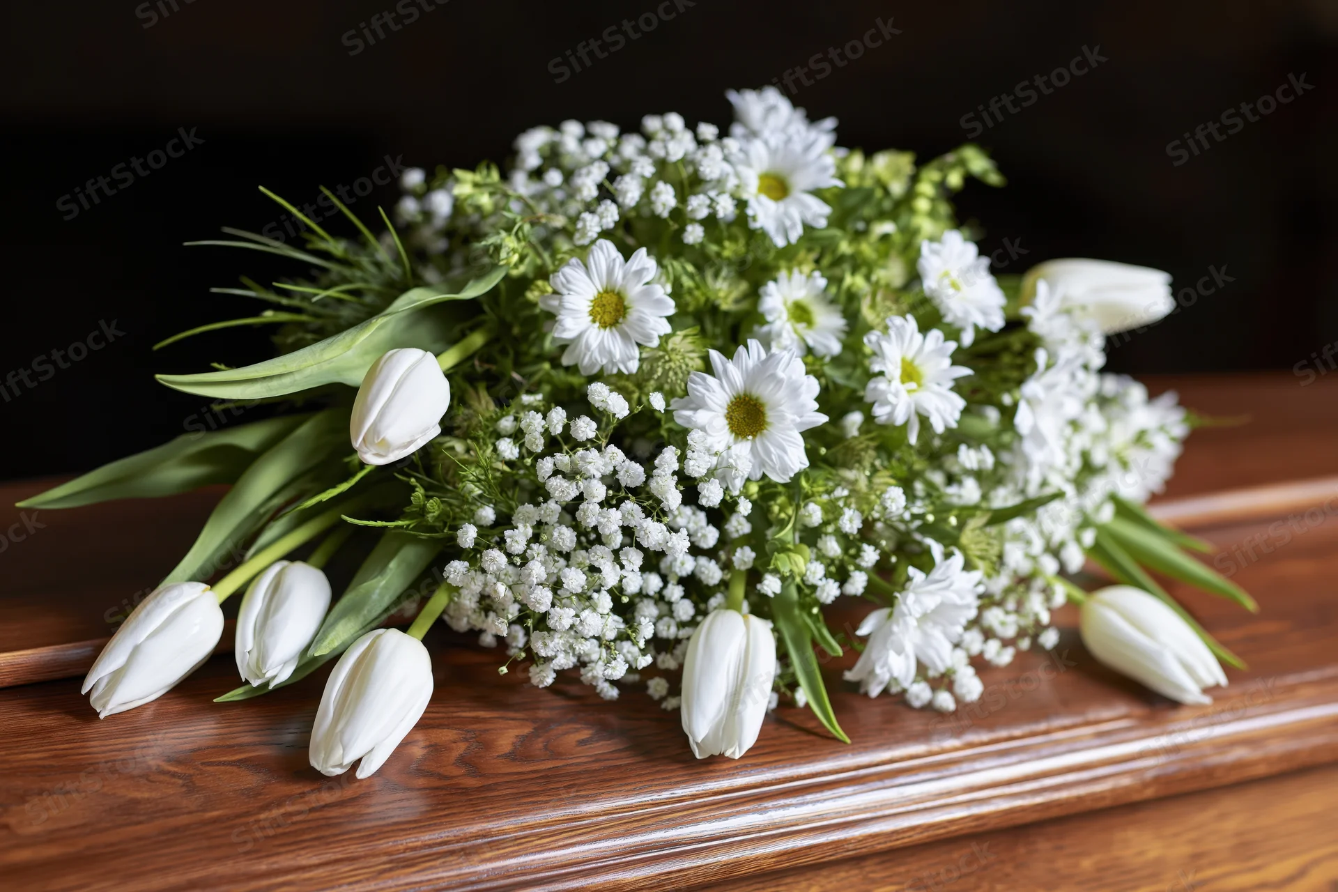 White tulips and daisies arranged as a funeral bouquet on a wooden coffin
