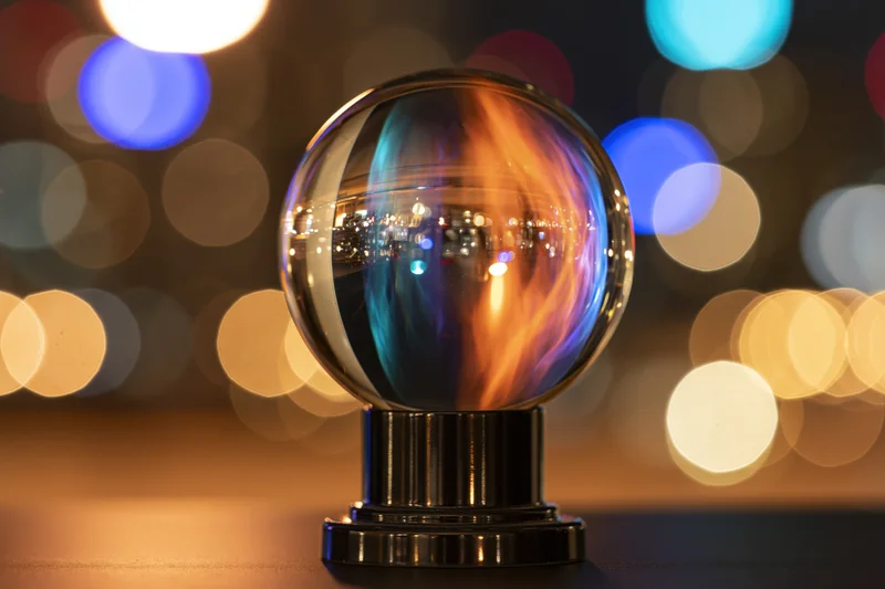 Glass crystal ball on black pedestal reflecting city lights at night