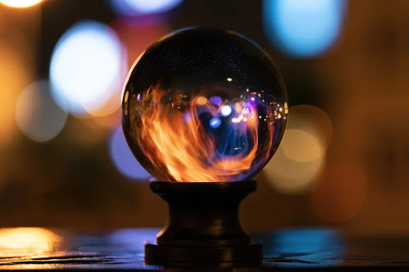 Glass crystal ball on black pedestal reflecting city lights at night on wooden surface