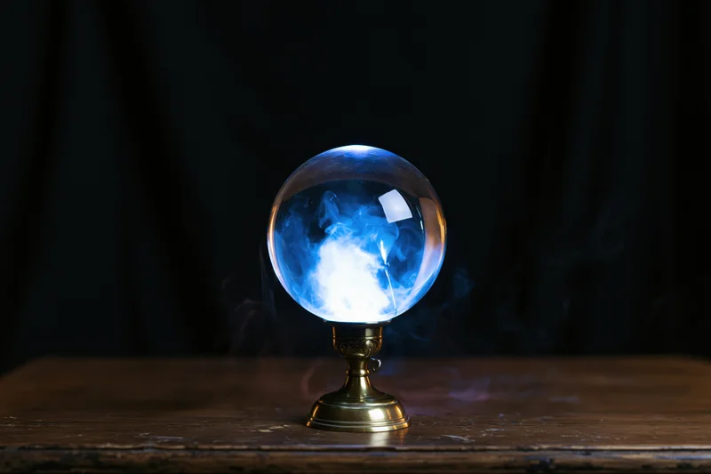 Glowing crystal ball with blue light and smoke on wooden table against dark background