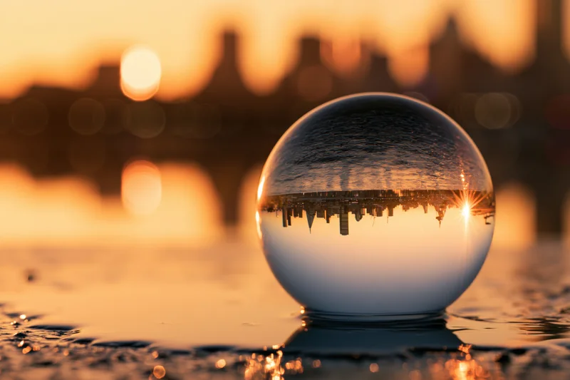 Crystal ball resting on wet surface reflecting city skyline at sunset