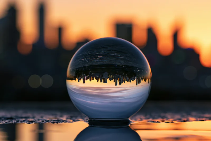 Crystal ball resting on wet surface reflecting city skyline at sunset