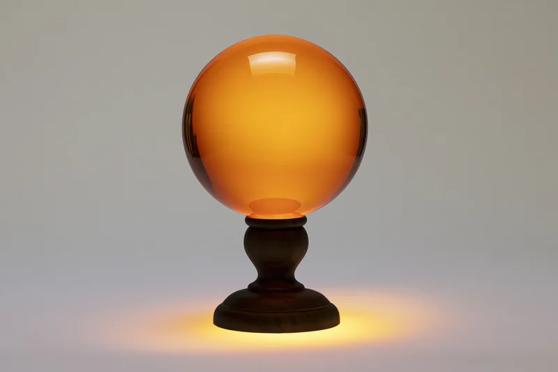 Glowing amber crystal ball on dark walnut wooden base emitting warm light