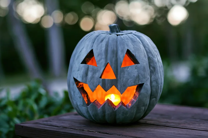Grey painted carved pumpkin jack-o-lantern glowing with candlelight on wooden table outdoors at evening
