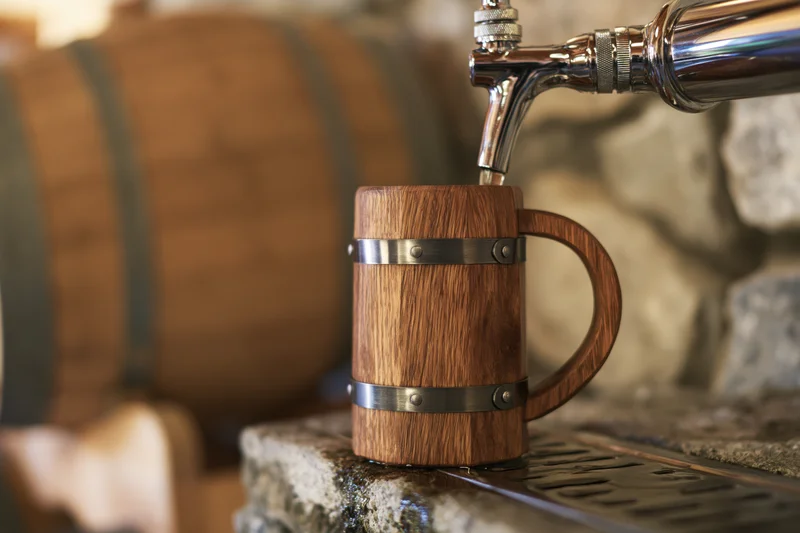Wooden beer mug being filled from a tap at a stone bar with a barrel in the background