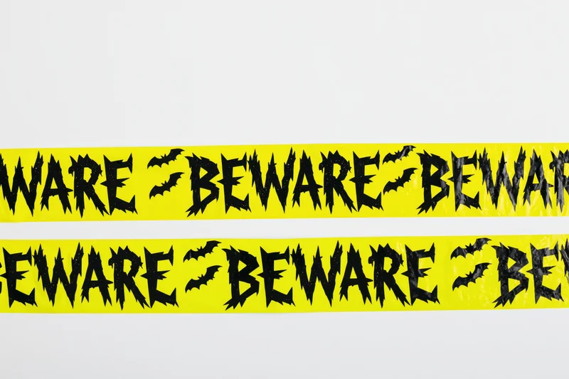 Bright yellow halloween caution tape with black beware text and bat symbols on white background