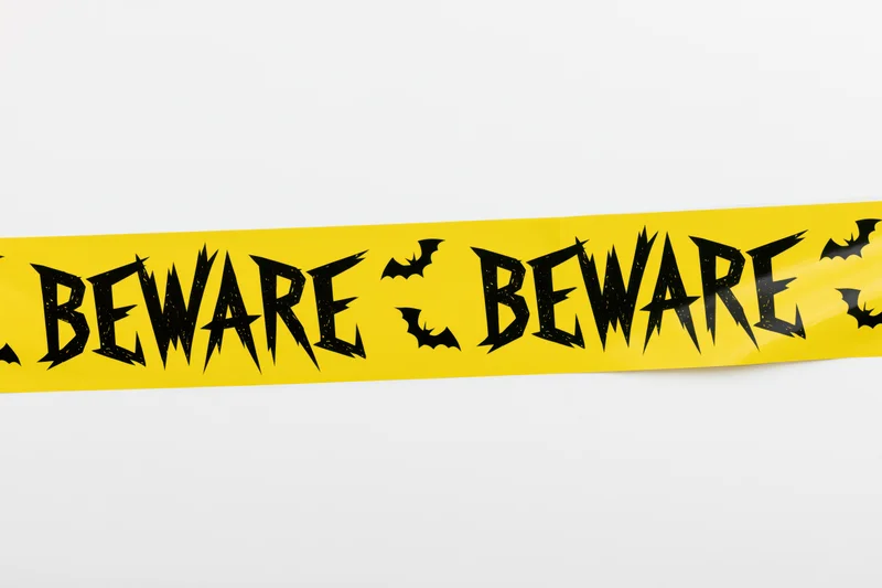 Yellow halloween caution tape with beware text and bat symbols on white background