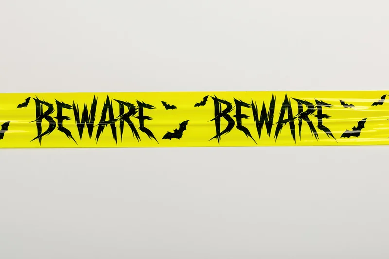 Bright yellow halloween caution tape with beware text and bat symbols on white background