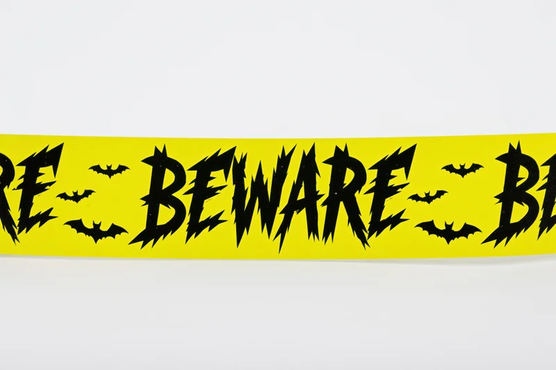 Bright yellow halloween caution tape with black beware text and bat symbols on white background