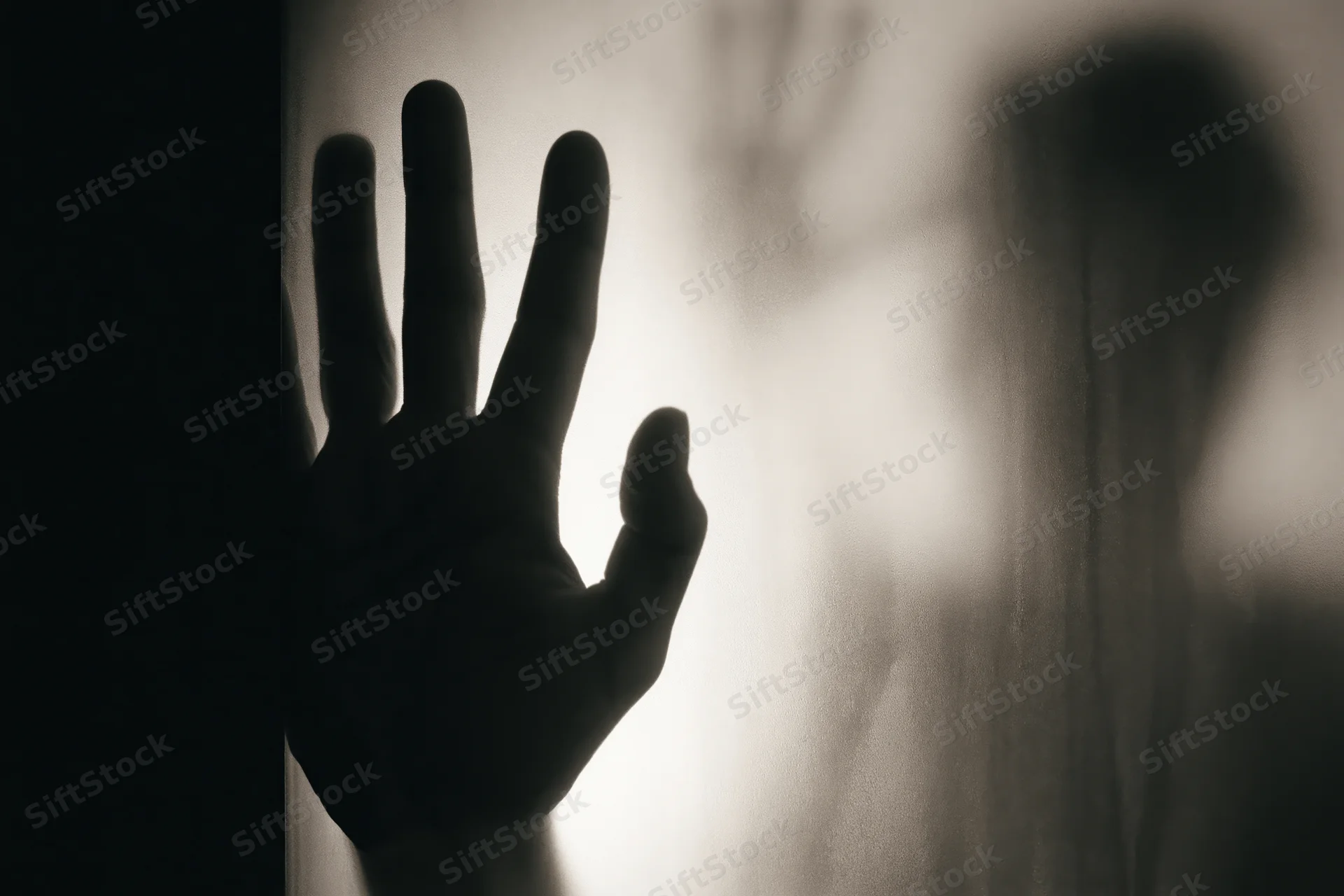 Hand pressed against frosted glass in shadowed interior