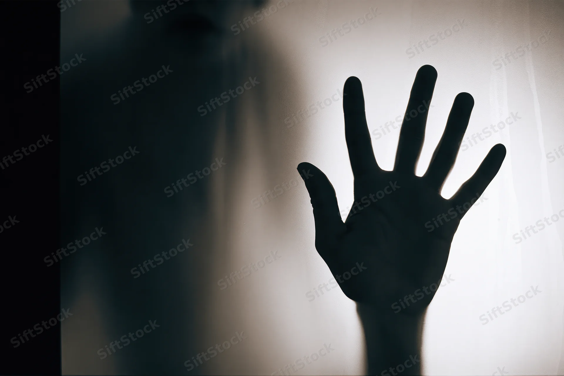 Silhouette of a hand pressed against frosted glass from behind, showing fingers spread and body blurred in shadow