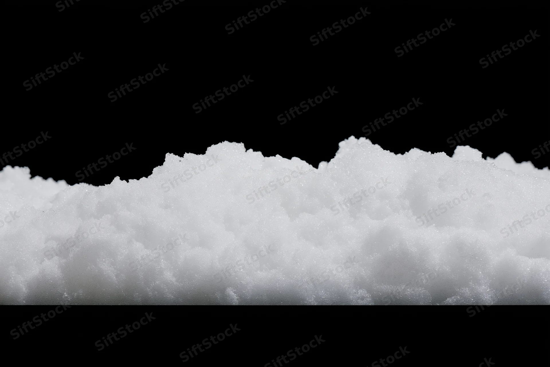 Low pile of loose white snow on flat surface against black background