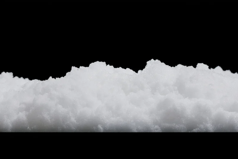 Low pile of loose white snow on flat surface against black background
