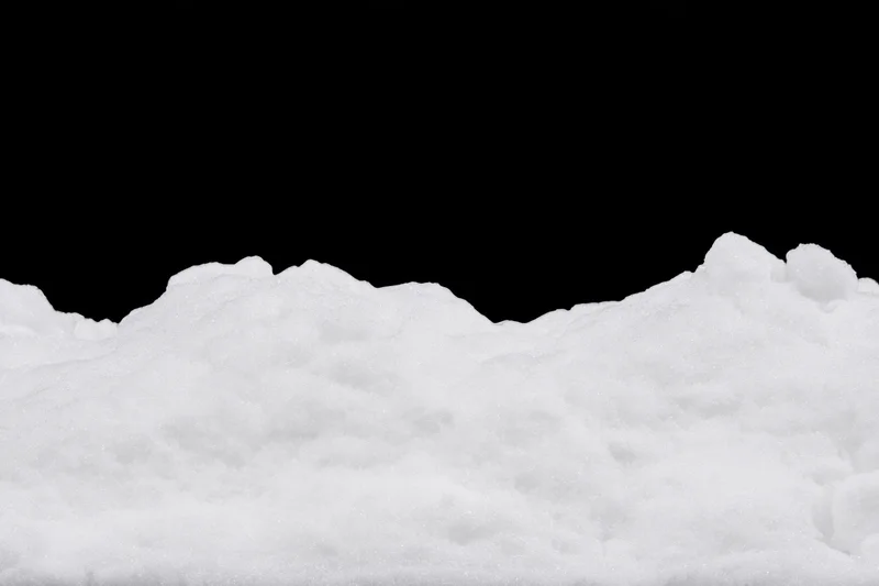 Low ridge of fresh white snow filling bottom third of frame against black background