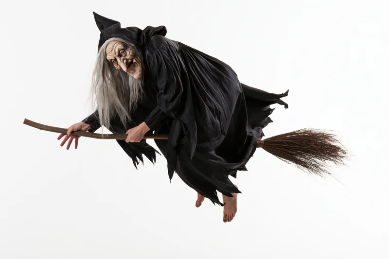 Old woman in witch costume flying on broomstick against white background