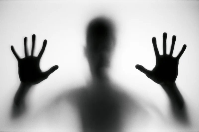 Silhouette of a person pressing hands and face against frosted glass