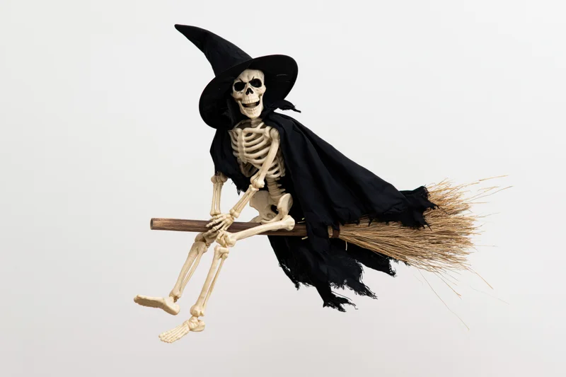 Skeleton wearing witch hat and black cape flying on broomstick against white background