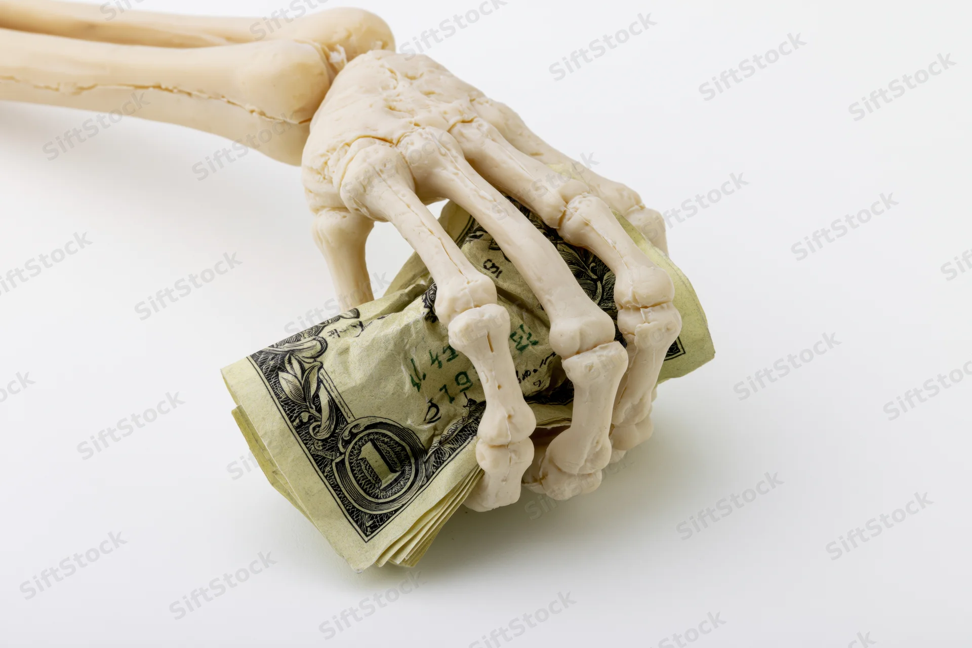 Skeleton hand gripping crumpled us dollar bills on white background