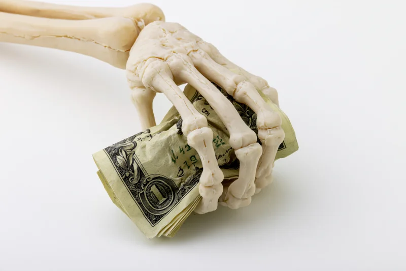 Skeleton hand gripping crumpled us dollar bills on white background