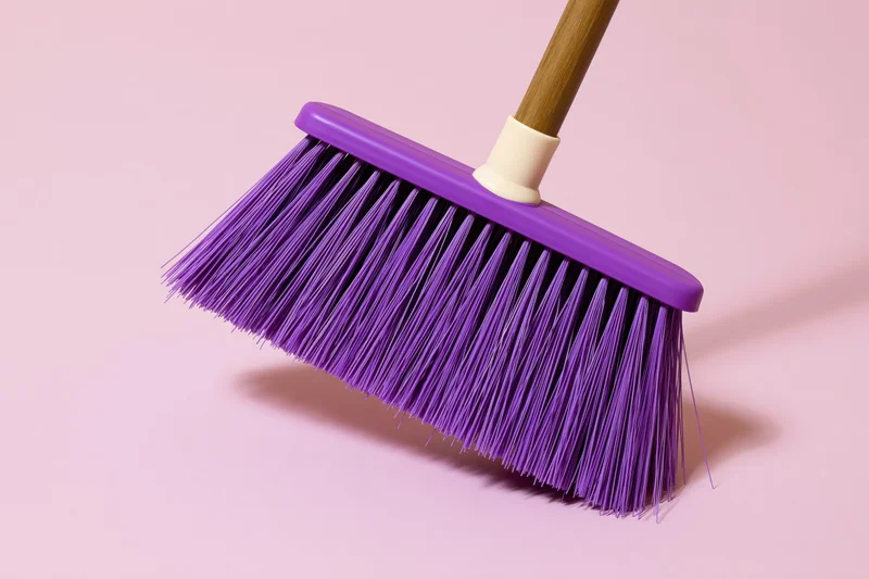 Purple plastic broom with dense synthetic bristles on a pink background