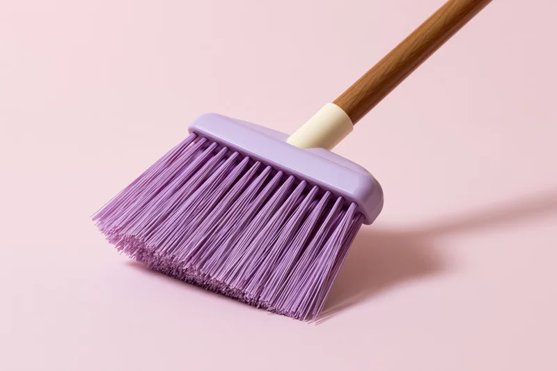 Purple plastic broom with dense synthetic bristles and wooden handle on pink background