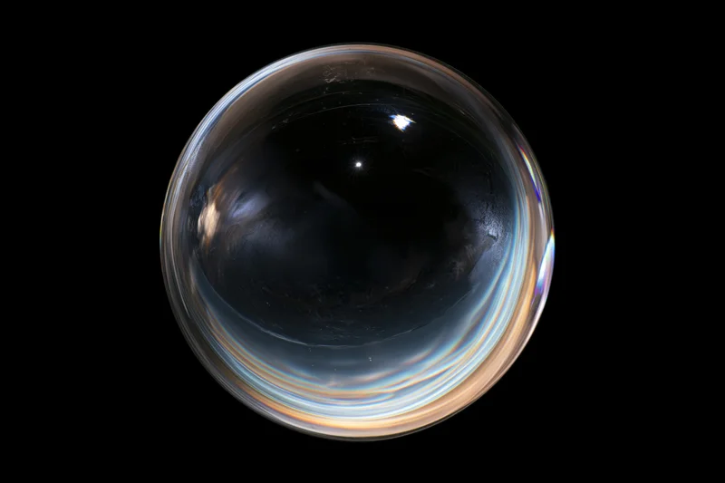 A clear glass sphere floating against a pure black background, reflecting light and showing iridescent colors on its surface
