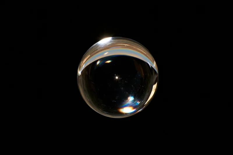 A clear glass sphere floating against a pure black background with light reflections and iridescent highlights