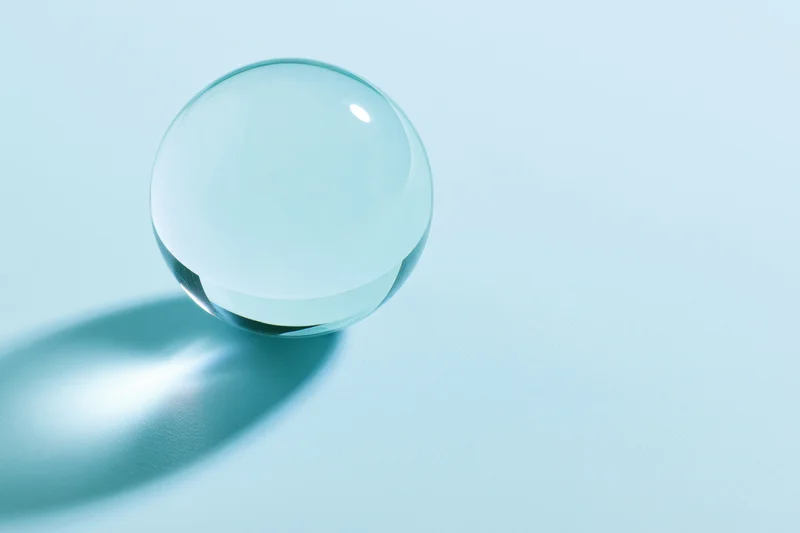 Clear glass sphere resting on pale blue surface with soft shadow