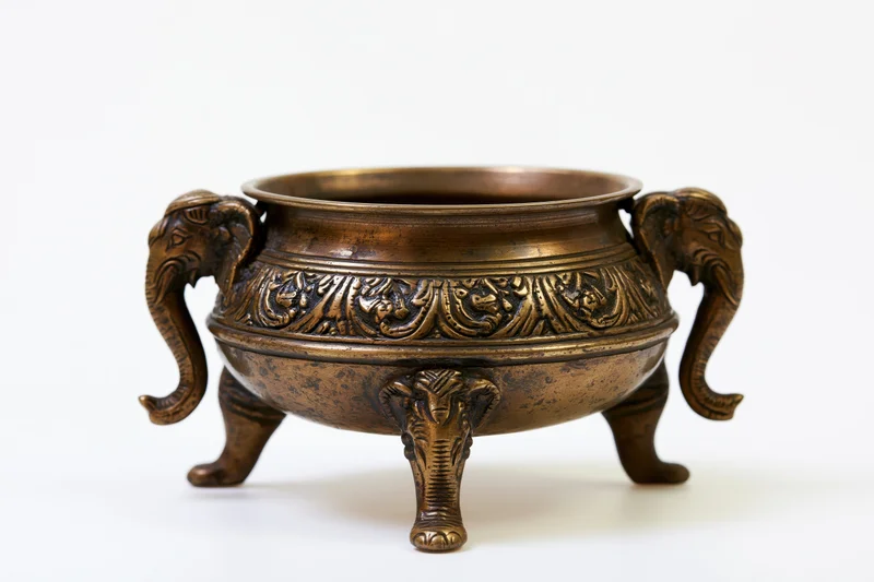 Antique brass incense burner with elephant head handles and carved details on white background