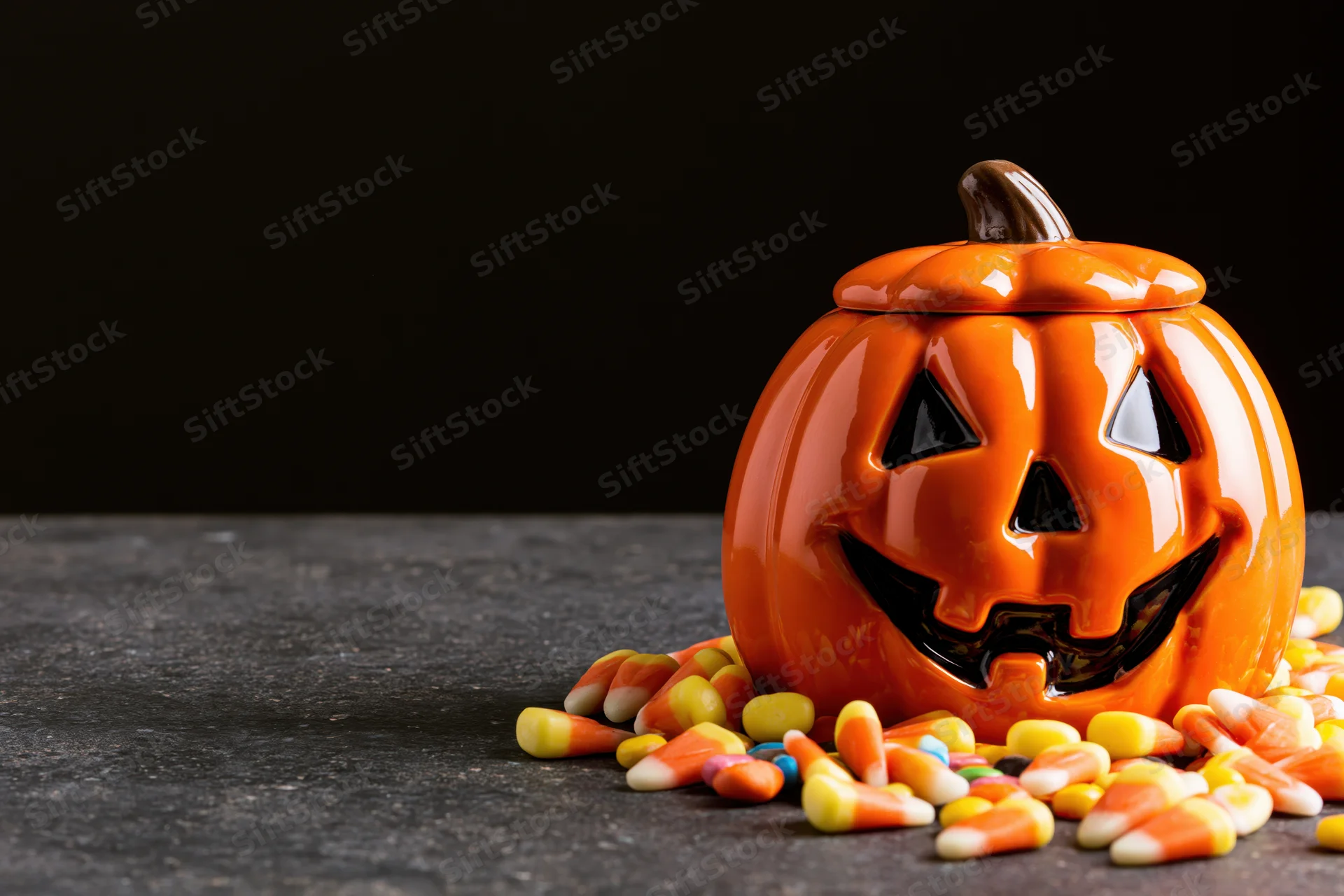 Ceramic jack-o-lantern decoration with scattered candy corn on dark surface