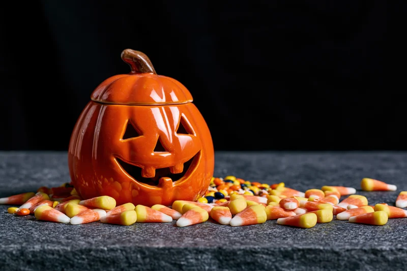 Ceramic jack-o-lantern decoration with scattered candy corn on dark surface