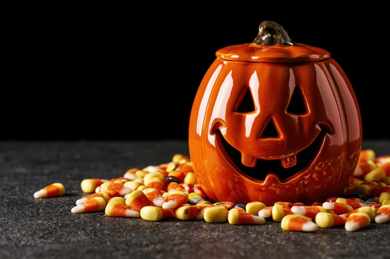 Ceramic jack-o-lantern decoration with scattered candy corn on dark surface