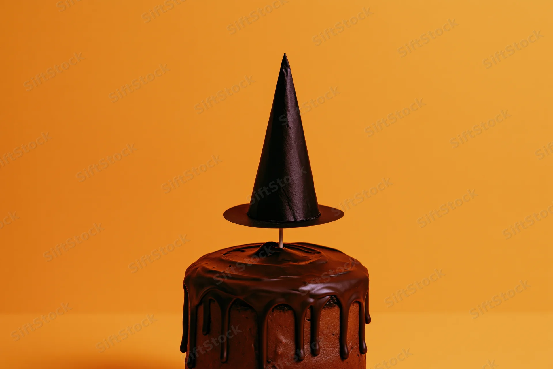 Chocolate-frosted cake with a paper witch hat on orange background