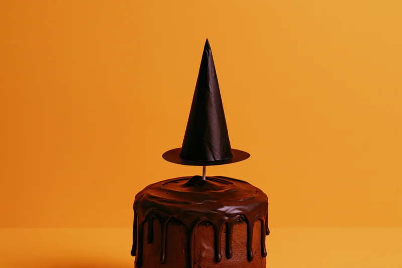 Chocolate-frosted cake with a paper witch hat on orange background