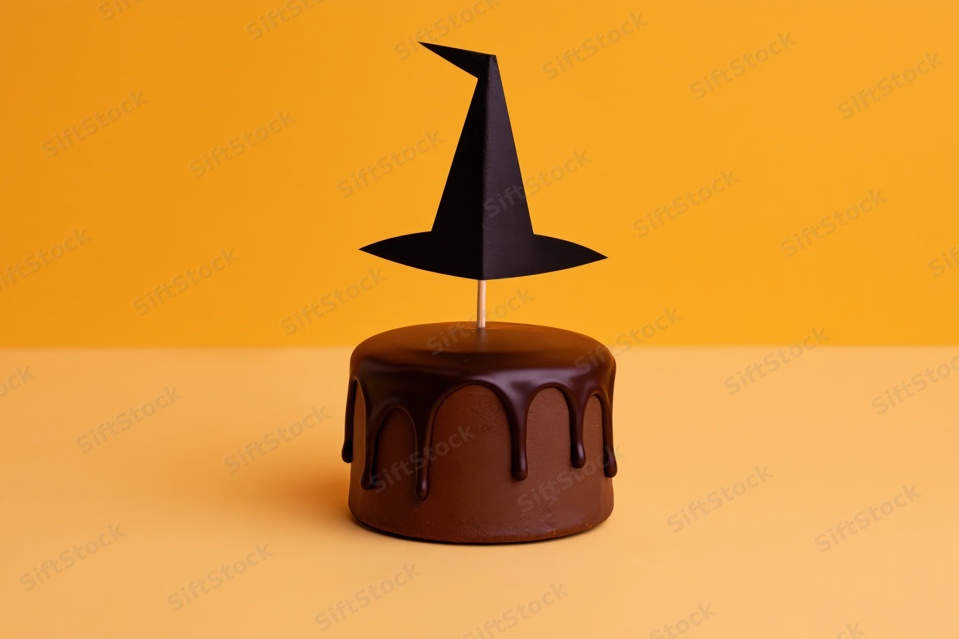 Chocolate-frosted cake with paper witch hat decoration on orange background
