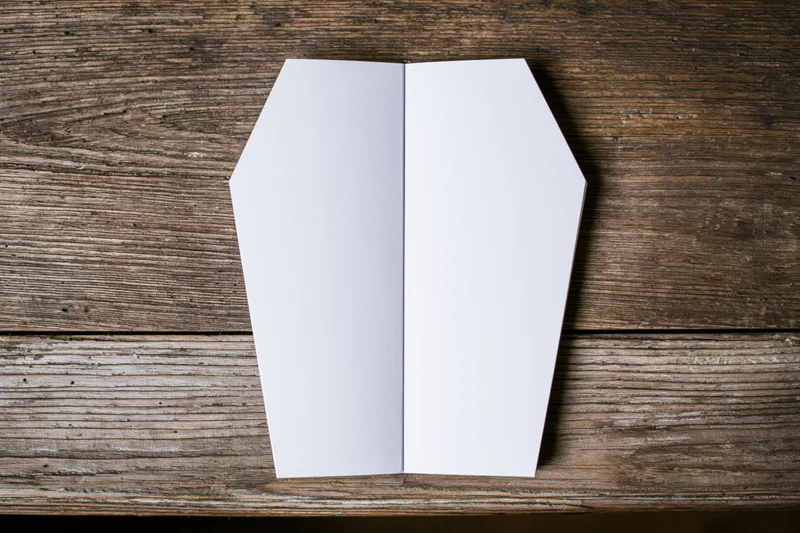 Open coffin-shaped blank white notepad on wooden table